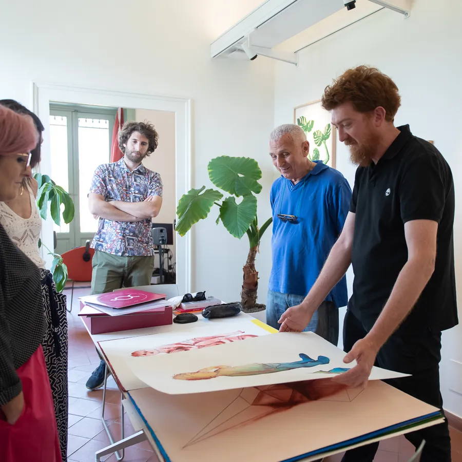 Un artista mostra una sua stampa ai partecipanti, appoggiata su un tavolo