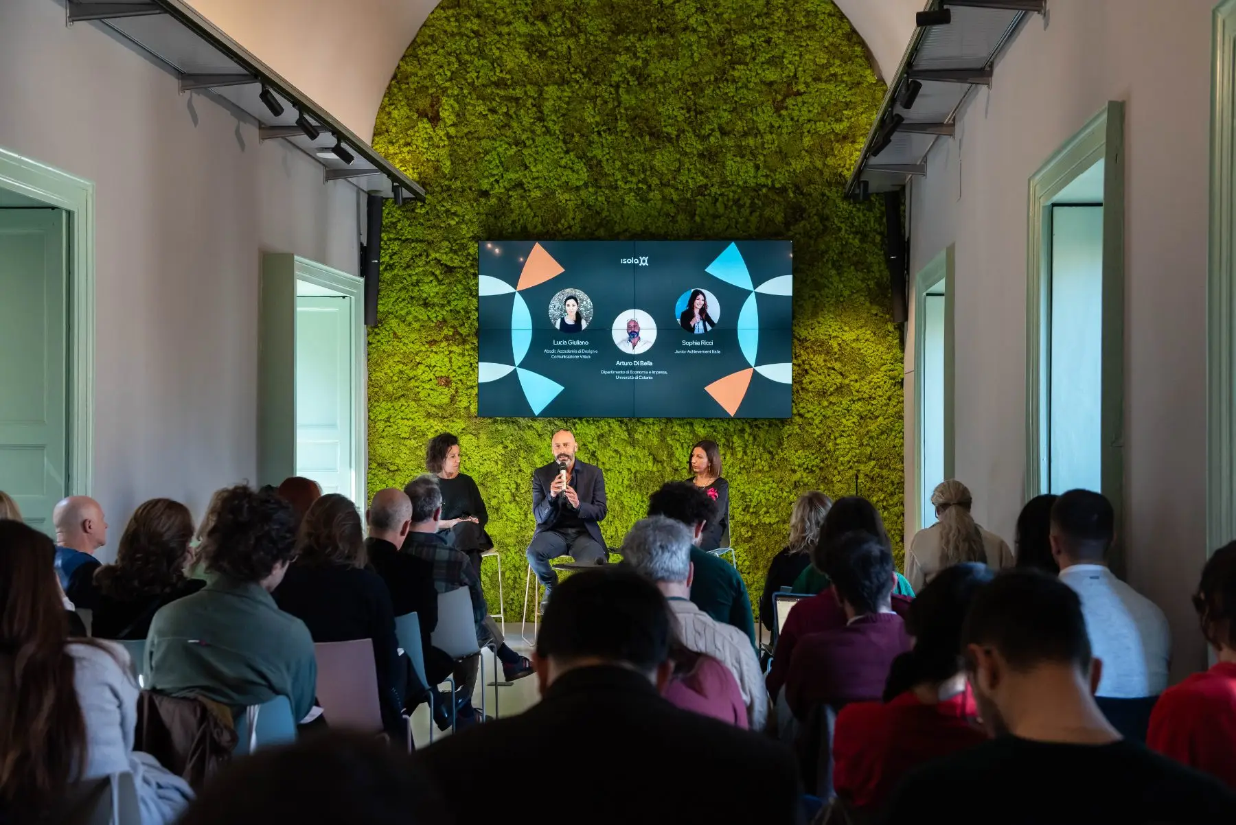 Il panel sulla creatività e l’impresa davanti alla parete verde della sala di Isola, con il pubblico in platea