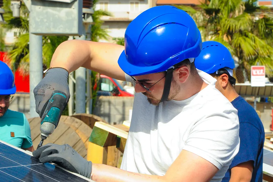 Un giovane con il casco blu fissa un pannello solare con un avvitatore