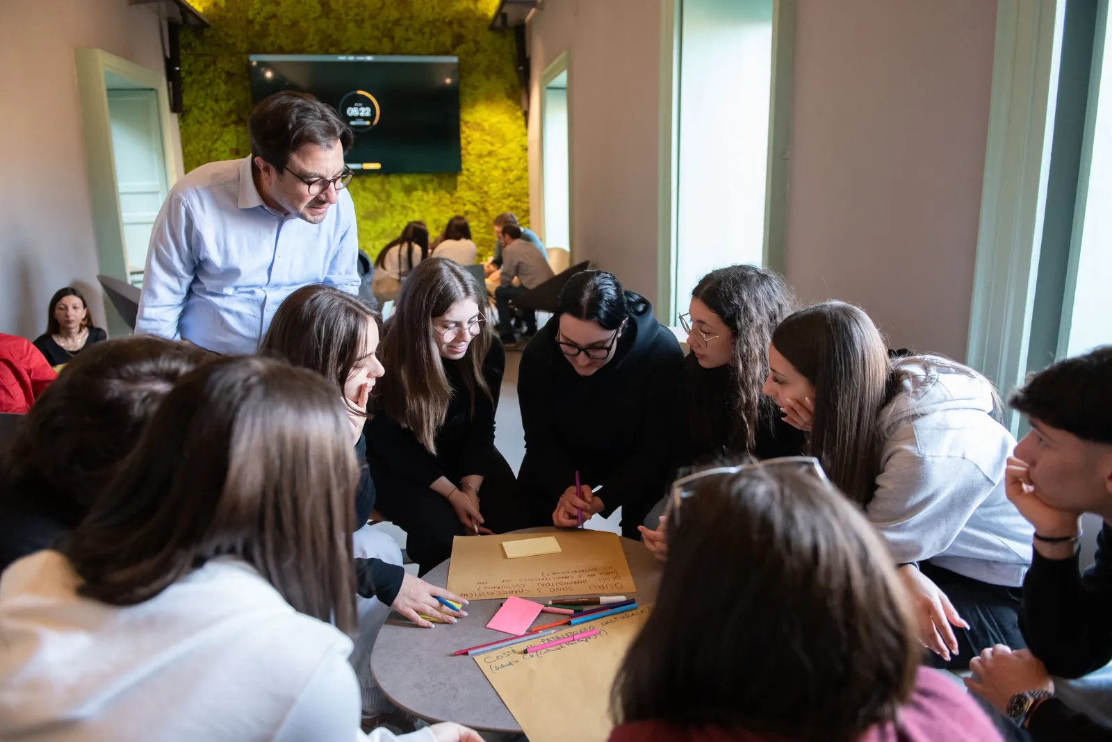Un gruppo di studentesse e studenti lavora attorno a un tavolo con cartelloni e pennarelli, seguito da un facilitatore, durante il National Ecosystem Forum italiano a Isola