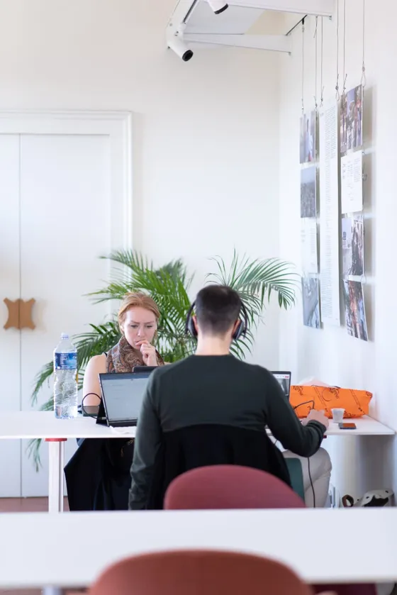 Due coworker a un tavolo condiviso, tra le piante e le stampe alle pareti
