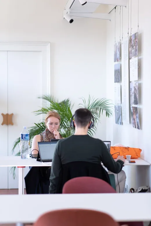 Due coworker a un tavolo condiviso, tra le piante e le stampe alle pareti