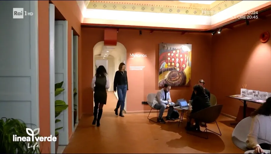 Fermo immagine della puntata di Rai 1: il corridoio di Isola con la sala Mykonos e persone al lavoro nell’area lounge